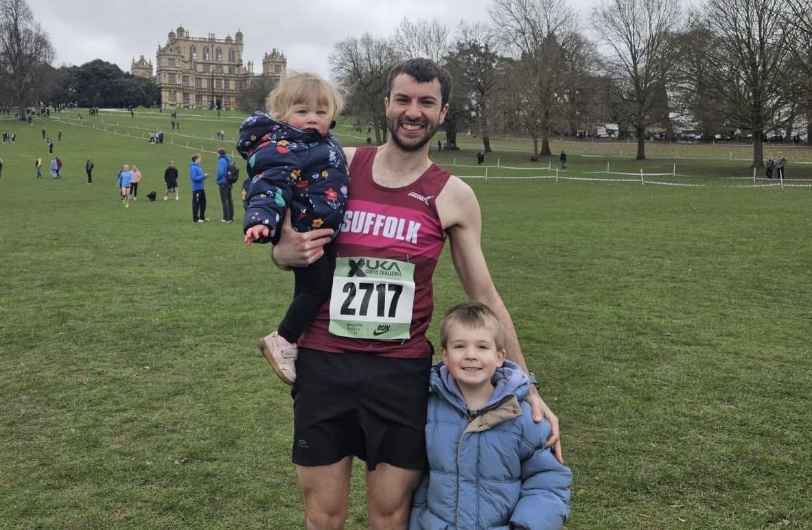 Man wearing running vest and shorts stood with his two small children in a parkland