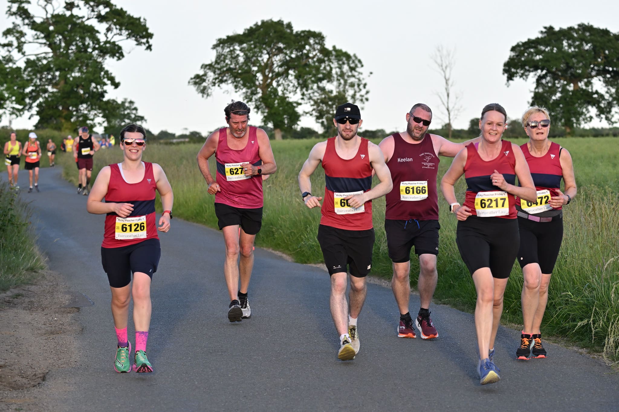 Group of male and female runners weating burgundy and blue running vests running on a country lane